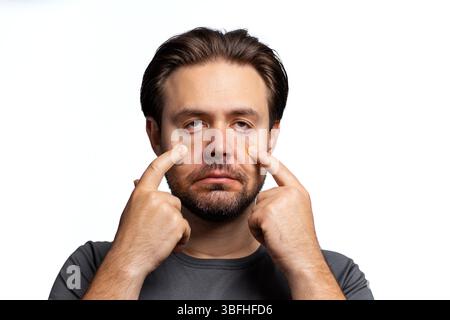 Junger Mann zieht die Augenlider nach unten, Porträt auf weißem Hintergrund Stockfoto