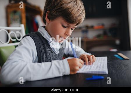 Junge Schüler, der seine Hausaufgaben zu Hause macht und am Tisch sitzt Stockfoto