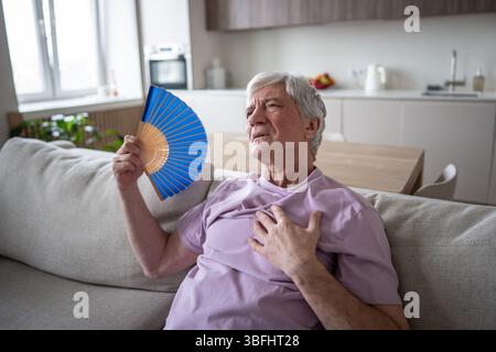 Schwitzender älterer Mann, der an erstickender Hitze, Übelkeit und Herzinfarkt zu Hause leidet Stockfoto