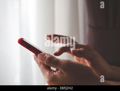 Nahaufnahme erwachsener Menschen Frauenhand mit rotem Smartphone, mit Fingerberührung auf dem Bildschirm, in dunklen Räumen, allein. Online Mobile Banking, Stockfoto