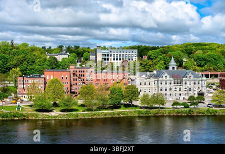 Blick über den Kennebec River in Richtung des historischen Stadtzentrums von Augusta in Maine, USA, mit Old Post Office, Gebäuden aus roten Backsteinen und mit Bäumen bewachsenen Hügeln unter teilweise bewölktem Himmel Stockfoto