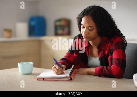 Konzentrierter schwarzer Schüler, der Notizen in der Küche zu Hause schreibt Stockfoto