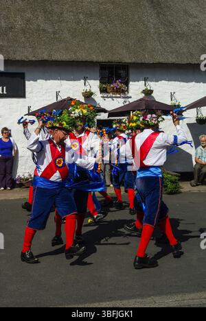 Morris-Tänzer in farbenfrohen blauen und roten Kostümen unterhalten Kunden vor dem Black Bull Pub, Etal Village, Northumberland, Großbritannien Stockfoto