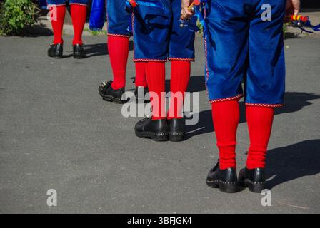Morris-Tänzer in farbenfrohen blauen und roten Kostümen unterhalten Kunden vor dem Black Bull Pub, Etal Village, Northumberland, Großbritannien Stockfoto