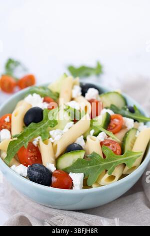 Mediterraner Pasta-Salat in einer Schüssel mit frischem Gemüse und Kräutern auf weißem Marmor Stockfoto