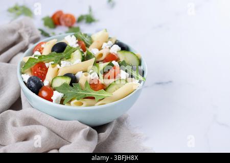 Mediterraner Pasta-Salat in einer Schüssel mit frischem Gemüse und Kräutern auf weißem Marmor Stockfoto
