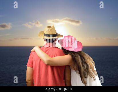 Ein Paar zu sich nehmen und die Sonne bei Sonnenuntergang am Strand beobachten Stockfoto