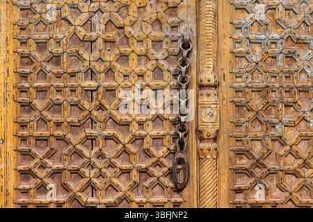 Detaillierte Ansicht einer Holztür mit komplizierten geometrischen Schnitzereien und einer Metallkette. Hebt traditionelle Handwerkskunst und kulturelles Design hervor Stockfoto
