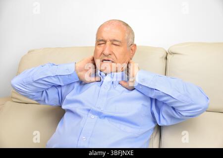 Ein älterer Mann leidet unter Nackenschmerzen, sitzt auf einem Sofa im Wohnzimmer zu Hause Stockfoto