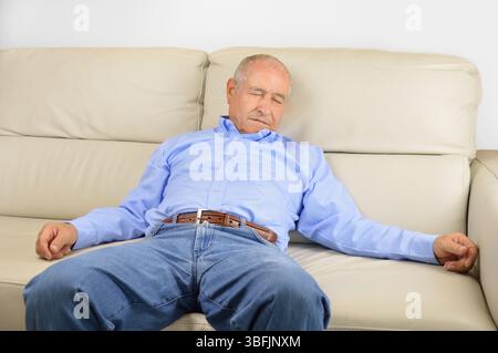 Senior-Mann ruht sich auf einer Couch zu Hause aus Stockfoto