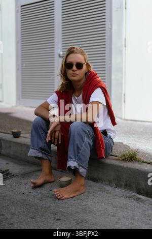 Die junge Frau sitzt auf dem Bürgersteig und trinkt Kaffee Stockfoto