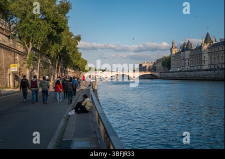 Menschen, die an einem sonnigen Nachmittag entlang der Promenade der seine in Paris spazieren gehen und sitzen, mit historischen Gebäuden im Hintergrund. Stockfoto