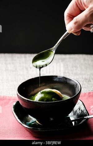 Von Hand tropfende Matcha-Sauce auf Vanilleeis Stockfoto