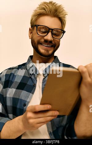 Junger Mann im karierten Hemd liest eifrig ein Buch, Brille an, strahlt eine helle Stimmung aus. Stockfoto