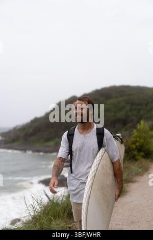 Junger Mann mit Surfbrett und Spaziergang zum Strand Stockfoto