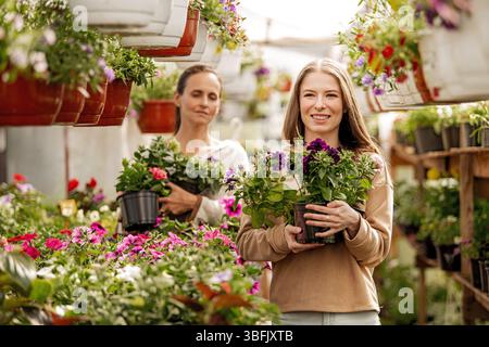Junge Frau mit Töpfen mit Blumensämlingen in einem Gewächshaus Stockfoto