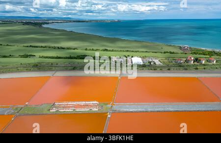 Aus der Vogelperspektive der farbenfrohen Salinen in der Nähe von Burgas, Bulgarien. Leuchtend rote und orangene Verdunstungsteiche stehen im Kontrast zu weißen Salzhaufen und türkisfarbenem Meer Stockfoto