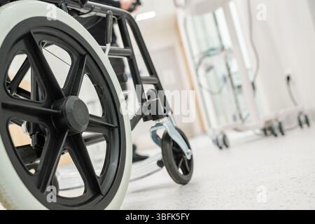 Eine Nahaufnahme eines Rollstuhlrads auf einem sauberen Krankenhausboden, mit medizinischen Wagen im Hintergrund während einer medizinischen Tätigkeit. Stockfoto