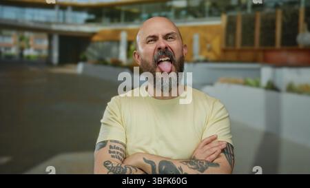 Glatze Mann mit Bart in lässigem Hemd, der Gesichtsausdrücke und Handgesten auf der städtischen Straße macht und charismatische und humorvolle Persönlichkeit in A c zeigt Stockfoto