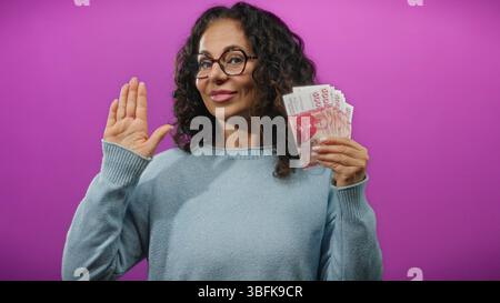 Frau, die isländische Kronen-Banknoten vor einem leuchtend violetten Hintergrund hält und damit finanzielle Verpflichtungen oder Versprechen symbolisiert. Stockfoto