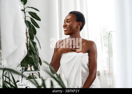 Frau genießt tagsüber einen Moment der Selbstpflege in einem hellen Badezimmer, umgeben von Pflanzen Stockfoto