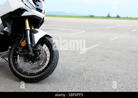 Nahaufnahme von Vorderrad, Federung und Scheibenbremse eines auf Asphalt geparkten Abenteuermotorrads mit modernem Motorraddesign und -Detail. Stockfoto