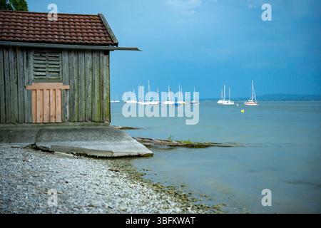 Ein Altes, Hölzernes Bootshaus Am Ufer Des Ammersees Im Abendlicht, Bayern, Deutschland. Segelboote Auf Dem Wasser. Stockfoto
