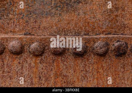 Extreme Nahaufnahme korrodierter Stahloberfläche mit horizontaler Nietreihe und Rostmuster Stockfoto
