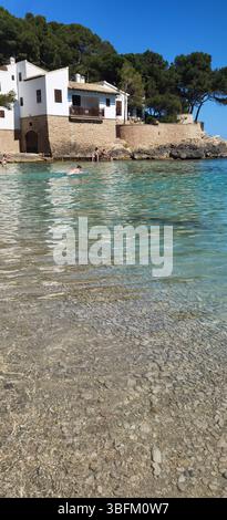 Cala Gat, Mallorca, Spanien; Juni 2025: Ein traditionelles mediterranes Haus steht friedlich zwischen türkisfarbenem Wasser und weichem rosa Sand, eingerahmt von Kiefern Stockfoto