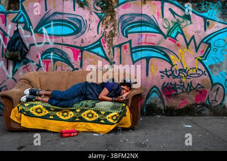 Ein kolumbianischer Drogenkonsument raucht Basuco – eine unraffinierte, schmutzige Kokainpaste –, während er auf einem weggeworfenen Sofa auf einer Straße in El Bronx, Medellín, Kolumbien liegt. Stockfoto