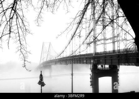 Aus der ätherischen Umarmung des Nebels erhebt sich eine einsame Brücke. Stockfoto