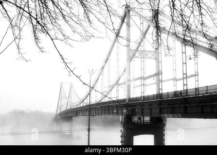 Aus der ätherischen Umarmung des Nebels erhebt sich eine einsame Brücke. Stockfoto