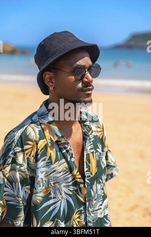 Junger Mann mit Sonnenbrille, hawaiianischem Hemd und Eimerhut, der Sommerurlaub an einem tropischen Strand genießt Stockfoto