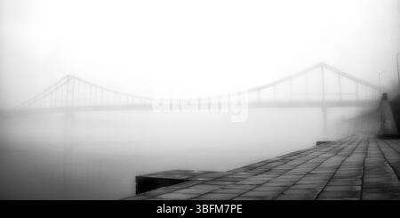 Aus der ätherischen Umarmung des Nebels erhebt sich eine einsame Brücke. Stockfoto