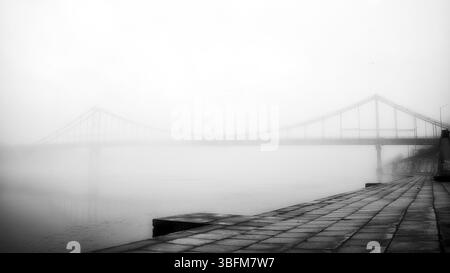 Aus der ätherischen Umarmung des Nebels erhebt sich eine einsame Brücke. Stockfoto