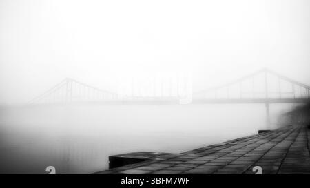 Aus der ätherischen Umarmung des Nebels erhebt sich eine einsame Brücke. Stockfoto