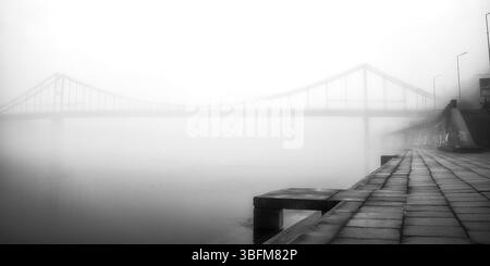 Aus der ätherischen Umarmung des Nebels erhebt sich eine einsame Brücke. Stockfoto