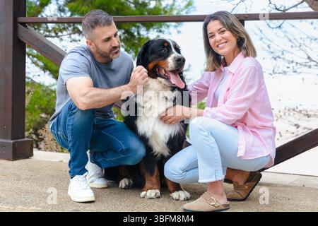 Ein lächelndes Paar mit Berner Sennenhund genießt im Frühling einen Moment im Freien Stockfoto