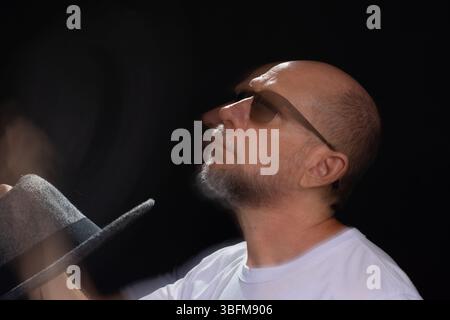 Künstlerisches Porträt eines bärtigen Glatzen-Mannes in weißem Hemd, der Bewegungen mit Armen und Händen verwischt. Schwarzer Hintergrund. Stockfoto