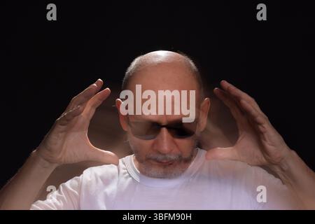 Künstlerisches Porträt eines bärtigen Glatzen-Mannes in weißem Hemd, der Bewegungen mit Armen und Händen verwischt. Schwarzer Hintergrund. Stockfoto