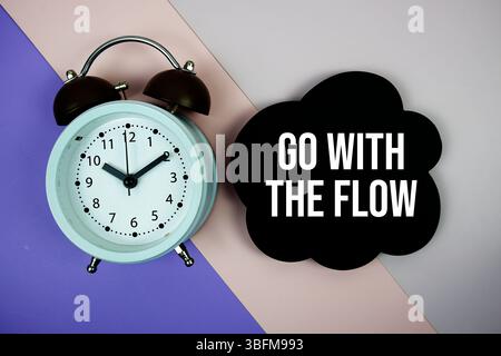 Verwenden Sie den Text „Flow“ auf der Sprechblase mit Wecker Draufsicht auf violettem geometrischem Hintergrund Stockfoto