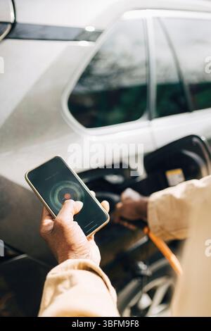 Hand auf Mann, der das Smartphone hält, während er die App benutzt, während er das Elektroauto auflädt Stockfoto