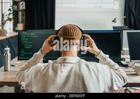 Rückansicht eines männlichen Computerprogrammierers, der im Büro kabellose Kopfhörer trägt Stockfoto
