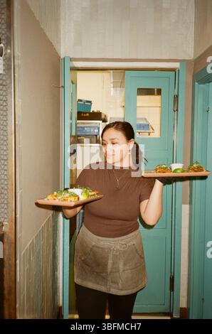 Eine junge Frau, die Essensbehälter hält, während sie aus der Küchentür kommt Stockfoto