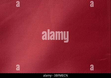 Tiefrotes Material mit feinen diagonalen Linien und weicher Textur, beleuchtet durch natürliches Licht in Innenräumen. Stockfoto