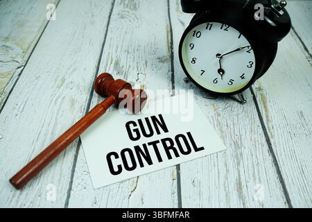 Gun Control Text auf Papierkarte mit Wecker und hölzerner Richter Gavel von oben auf hölzernem Hintergrund Stockfoto