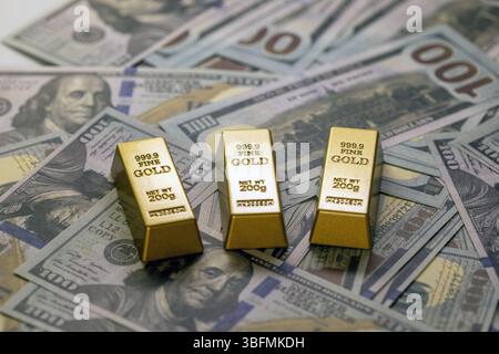 Drei Goldbarren ruhen auf hundert Dollar-Scheine, die Wohlstand und Investitionen symbolisieren. Goldbarren sind mit ihrem Gewicht und ihrer Reinheit gekennzeichnet, Highli Stockfoto