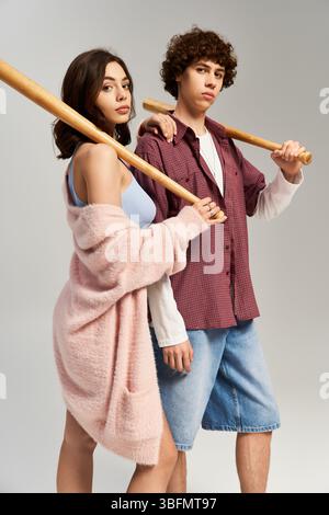 Das modische junge Paar steht zusammen mit Baseballschlägern und zeigt ihren trendigen Stil und ihre Liebe. Stockfoto