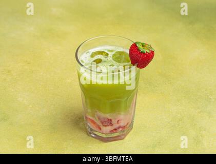 Eismatcha Latte mit Erdbeerpüree und Eiswürfeln, dekoriert mit frischer Erdbeere in einem Glas auf grünem Hintergrund Stockfoto