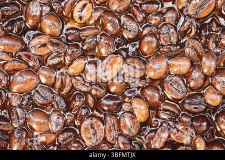Kaffeebohnen in Epoxidharz. Künstlerischer Texturhintergrund. Dunkelbraun gerösteter Kaffee. Kreative dekorative Oberfläche. Glänzende Bohnen, haltbar gemacht. Stockfoto